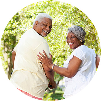 a photo of a retired couple in a walk in a park looking back over their shoulders and smiling at the camera